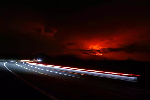 In this long camera exposure, cars drive down Saddle Road as Mauna Loa erupts in the distance, Monday, Nov. 28, 2022, near Hilo, Hawaii. Mauna Loa, the world's largest active volcano erupted Monday for the first time in 38 years. (AP Photo/Marco Garcia)