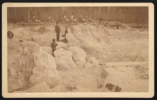 Photograph shows two white men overseeing African American men hammering boulders as others walk with wheelbarrows in a shallow pit phosphate mine, Dunnellon, Florida, 1890. (Library of Congress via AP)