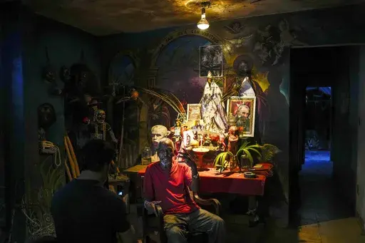 Juan Gonzalez sits next to his altar adorned Santeria and Catholic deities along with a photo of the late Cuban leader Fidel Castro, at his home in El Cobre, Cuba, Feb. 10, 2024. Diverse beliefs can be found mixed together on altars in Cuban homes, with the Virgin Mary sharing space with a ceramic Buddha and a warrior spirit from the Afro-Cuban faith. (AP Photo/Ramon Espinosa, File)