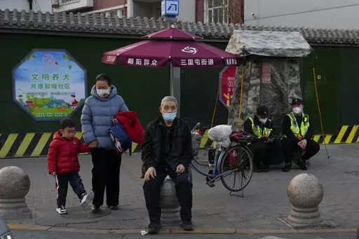 Residents wait to cross a road near members of the Chaoyang militia on duty in Beijing, Monday, March 6, 2023. Chinese economic officials expressed confidence Monday they can meet this year's growth target of "around 5%" by generating 12 million new jobs and encouraging consumer spending following the end of anti-virus controls that kept millions of people at home. (AP Photo/Ng Han Guan)