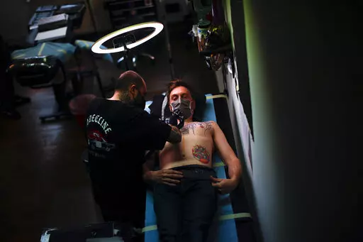 A man, wearing a protective face mask to prevent the spread of coronavirus, is tattooed at Paul and Friends tattoo parlour in downtown Brussels, March 26, 2021. The European Union is imposing restrictions on the inks that tattoo artists can use as of Wednesday, Jan. 5, 2022. The EU says it is a necessary move to protect the health of consumers because thousands of chemical elements now in use can cause anything from allergic reactions to cancer. The tattoo industry complains it is unfairly targe