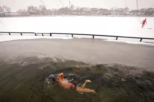 A man swims in the half-frozen water at the Shichahai Lake during a snow fall in Beijing, Sunday, Feb. 13, 2022. According to some of the local residents, swimming in the freezing water leads to health. (AP Photo/Andy Wong)