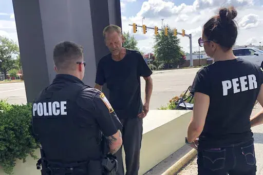 Chesterfield Patrol Officer Travis Adams, left, and peer recovery specialist Joy Bogese, right, talk with Adam Hall as part of Project Recover, in Chesterfield County, Va., Monday, Aug., 29, 2022. Project Recover is a program that embeds recovering addicts with police and ambulance crews in central Virginia to respond to overdose calls and to go on patrol to reach out to people struggling with drug addiction to try to get them into treatment programs. (AP Photo/Denise Lavoie)