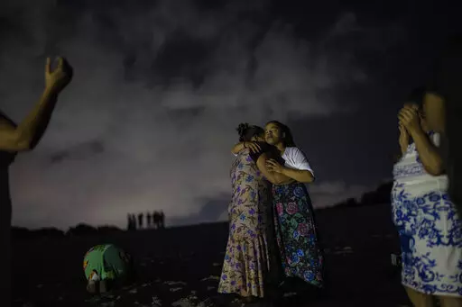 Mag Oliveira embraces her daughter Najla as they pray in an area of the Abaete dune system, on a steep rise of sand evangelicals have come to call the "Holy Mountain", in Salvador, Brazil, late Friday night, Sept. 16, 2022. Evangelicals have been converging on the dunes for some 25 years but especially lately, with thousands now coming each week to sing, pray and enter trancelike states to commune with God.(AP Photo/Rodrigo Abd)