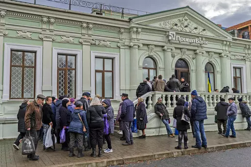 Residents queue at a bank branch in Kherson, southern Ukraine, Nov. 21, 2022. Even as Ukraine celebrates recent battlefield victories, its government faces a looming challenge on the financial front: how to pay the enormous cost of the war effort without triggering out-of-control price spikes for ordinary people or piling up debt that could hamper postwar reconstruction. (AP Photo/Bernat Armangue, File)