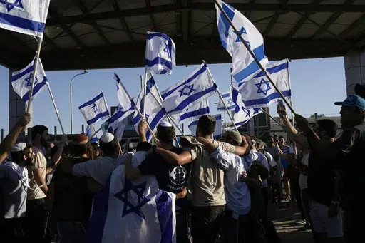 Protesters wave Israeli national flags in support of soldiers being questioned for detainee abuse, outside of the Sde Teiman military base, Monday, July 29, 2024. The Israeli military said Monday it was holding nine soldiers for questioning following allegations of "substantial abuse" of a detainee at a shadowy facility where Israel has held Palestinian prisoners throughout the war in Gaza. (AP Photo/Tsafrir Abayov)