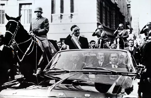 Chilean President Salvador Allende salutes from an open vehicle as General Augusto Pinochet rides on horseback at left in Santiago, Chile, May 21, 1972. (AP Photo/File)