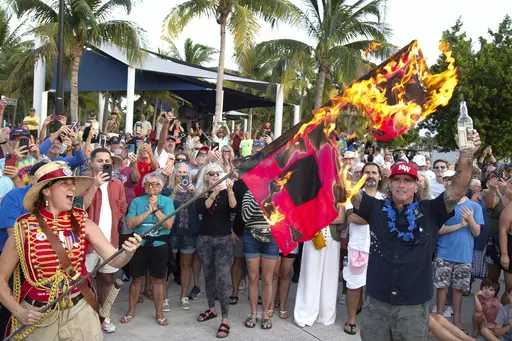 In this photo provided by the Florida Keys News Bureau, Jai Somers, left, holds hurricane warning flags aloft as they burn after being doused with rum by Paul Menta, right, to mark the end of the 2023 Atlantic hurricane season Thursday, Nov. 30, 2023, in Key West, Fla. According to the National Hurricane Center, this year's above-normal Atlantic hurricane season was characterized by record warm Atlantic Ocean sea surface temperatures and a strong El Nino. The Atlantic basin saw 20 named storms i