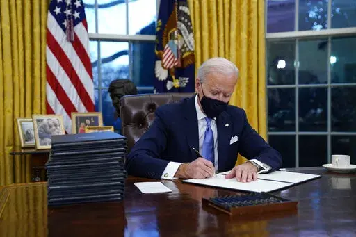 In this Jan. 20, 2021, file photo, President Joe Biden signs his first executive order in the Oval Office of the White House in Washington. Biden laid out an ambitious agenda for his first 100 days in office, promising swift action on everything from climate change to immigration reform to the coronavirus pandemic. Key members of the White House Environmental Justice Advisory Council say one year into the Biden Administration's commitment that 40% of all benefits from climate investment go to d