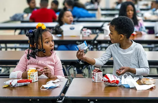 First graders, from left, Kendal Kates and Ryan Kenney are excited about the contents of their boxed lunches at Langley K-8 School, Dec. 23, 2021, in the Sheraden neighborhood in Pittsburgh. The Biden administration has issued transitional standards for school lunches that are meant to get cafeterias back on a healthier course as they recover from pandemic and supply chain disruptions.  The “bridge” rule announced by the U.S. Agriculture Department on Friday extends emergency flexibilities f