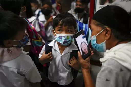 A boy talks to his mother from a smartphone during the opening of classes at the San Juan Elementary School in metro Manila, Philippines on Monday, Aug. 22, 2022. Millions of students wearing face masks streamed back to grade and high schools across the Philippines Monday in their first in-person classes after two years of coronavirus lockdowns that are feared to have worsened one of the world's most alarming illiteracy rates among children. (AP Photo/Aaron Favila)