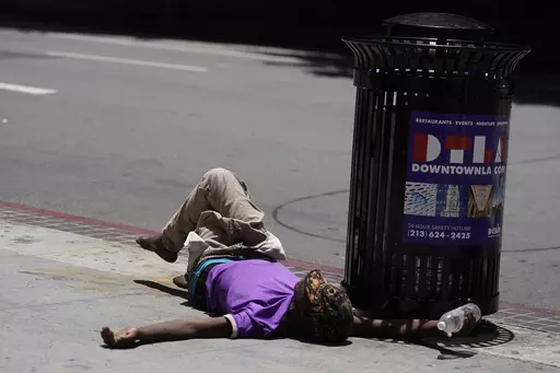 A homeless person lies on the sidewalk while holding a water bottle, Sunday, July 2, 2023, in downtown Los Angeles. Excessive heat warnings remain in place in many areas across the U.S. and are expected to last at least through Monday. (AP Photo/Damian Dovarganes, File)