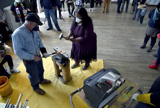 Sharletta Evans, right, whose 3-year-old son, Casson, was killed in a drive-by shooting in 1995, helps Fred Martin, a volunteer blacksmith for the nonprofit group RAWtools, hammer a rifle barrel into a garden tool at a church in Denver, Sunday, Jan. 16, 2022. The Colorado Springs-based group transforms guns into garden tools and draws inspiration from the Bible verse, "They shall beat their swords into plowshares and their spears into pruning hooks." (AP Photo/Thomas Peipert)