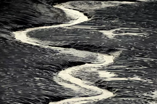 A channel flows through the mud flats along the Seward Highway and Turnagain Arm in Alaska on Oct. 25, 2014. Authorities said, a 20-year-old man from Illinois who was walking Sunday evening, May 21, 2023, on tidal mud flats with friends in an Alaska estuary, got stuck up to his waist in the quicksand-like silt and drowned as the tide came in before frantic rescuers could extract him. (Bob Hallinen/Anchorage Daily News via AP)