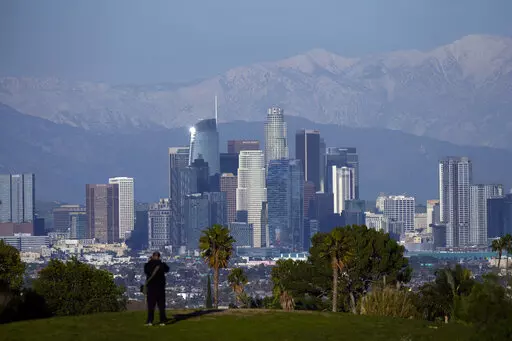 A visitor takes in a view of the city's skyline under the snow-covered San Gabriel mountains after a series of storms Thursday, March 2, 2023, in Los Angeles. (AP Photo/Marcio Jose Sanchez)