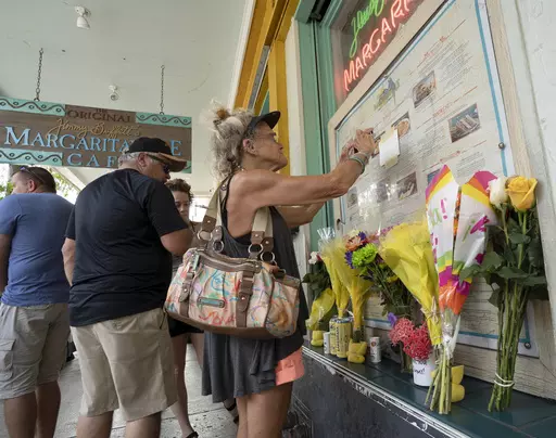 In this photo provided by the Florida Keys News Bureau, Susan Hudnall pins a condolence note about Jimmy Buffett's passing to the front window of the Margaritaville Cafe in Key West, Fla., Saturday, Sept. 2, 2023, in Key West, Fla. Buffett, who popularized beach bum soft rock with the escapist Caribbean-flavored song “Margaritaville” and turned that celebration of loafing into a billion-dollar empire of restaurants, resorts and frozen concoctions, died Friday, Sept 1. He was 76. Hudnall, a v