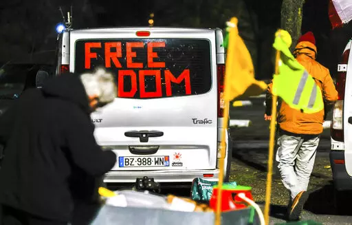 People walk by vehicles with banners and flags parked outside the city center of Brussels, early Monday, Feb. 14, 2022. Authorities in France and Belgium have banned road blockades threatened by groups organizing online against COVID-19 restrictions. The events are in part inspired by protesters in Canada. (AP Photo/Olivier Matthys)