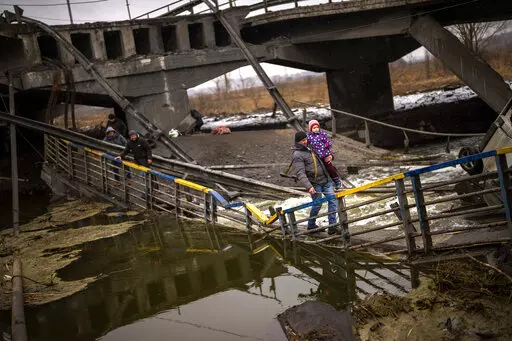 Local militiaman Valery, 37, carries a child as he helps a fleeing family across a bridge destroyed by artillery, on the outskirts of Kyiv, Ukraine, Wednesday, March 2. 2022.  Russian forces have escalated their attacks on crowded cities in what Ukraine's leader called a blatant campaign of terror. (AP Photo/Emilio Morenatti)