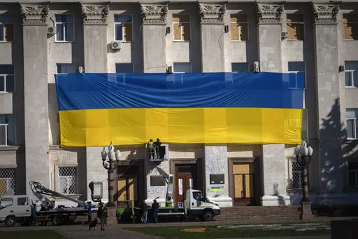 Municipal workers wearing protective vests and helmets decorate the wall of the regional administration building with a huge national flag to mark one year since the Ukrainian troops cleared the city from the Russian army, in Kherson, Ukraine, Friday, Nov. 10, 2023. (AP Photo/Efrem Lukatsky)