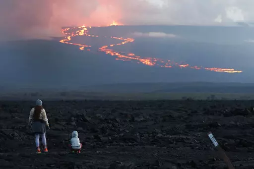 Spectators watch the lava flow down the mountain from the Mauna Loa eruption, Nov. 29, 2022, near Hilo, Hawaii. On Wednesday, Dec. 7, the lava from Mauna Loa, was 1.8 miles from Saddle Road, also known as Route 200 or Daniel K. Inouye Highway, scientists with the U.S. Geological Survey said. (AP Photo/Marco Garcia, File)