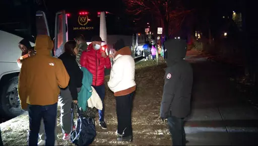 This image provided by WJLA shows migrant families as they get on to a bus to transport them from near the Vice President's residence to an area church after they arrived in Washington, Saturday, Dec. 24, 2022. Local organizers in Washington say three buses of recent migrant families arrived from Texas near the home in record-setting cold on Christmas Eve. Texas authorities have not confirmed their involvement. (WJLA via AP)