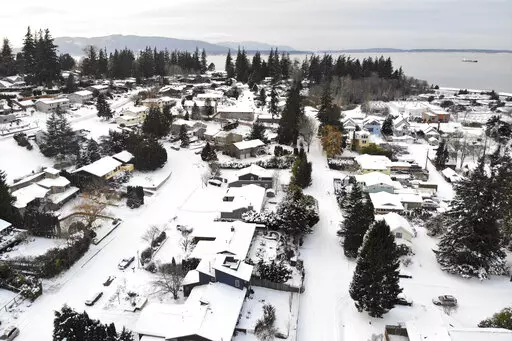 In this photo taken from a drone, snow covers streets, sidewalks and homes where nearly a foot of snow fell over the weekend, Monday, Dec. 27, 2021, in a neighborhood near Bellingham Bay in Bellingham, Wash. Emergency warming shelters were opened throughout western Washington and Oregon as temperatures plunged into the teens and forecasters said an arctic blast would last for several days. (AP Photo/Elaine Thompson)
