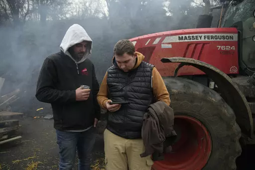 Farmers watch French Prime Minister Gabriel Attal on a smartphone, announcing new measures for farmers, on a blocked highway, Thursday, Feb.1, 2024 in Chilly-Mazarin, south of Paris. Protests have been held across the EU for most of the week and hundreds of angry farmers driving heavy-duty tractors arrived at European Union headquarters, bent on getting their complaints about excessive costs, rules and bureaucracy heard and fixed by EU leaders at a summit Thursday in Brussels, Belgium. (AP Photo