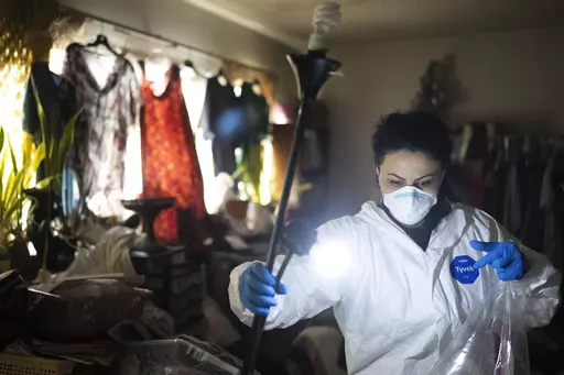 Wearing a protective suit, Arusyak Martirosyan, an investigator with the Los Angeles County Public Administrator's office, turns on a lamp while searching through a one-bedroom apartment in Los Angeles, Thursday, Nov. 16, 2023, for clues that might lead to finding family members or relatives of a tenant who died in the hospital with no apparent next of kin. (AP Photo/Jae C. Hong)