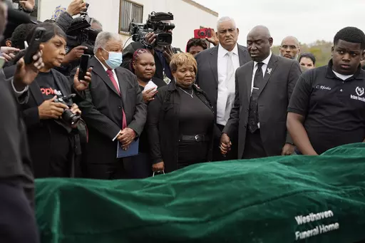 Civil rights attorney Ben Crump, center right, Bettersten Wade, center, mother of Dexter Wade, a 37-year-old man who died after being hit by a Jackson, Miss., police SUV driven by an off-duty officer, watches her son's body transferred to a mortuary transport after being exhumed from a pauper's cemetery near the Hinds County Penal Farm in Raymond, Monday, Nov. 13, 2023. After men in near Mississippi's capital were buried in a pauper’s cemetery without their relatives’ knowledge, the U.S. Jus