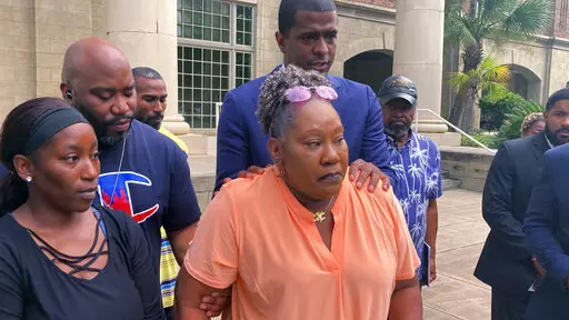 Betty James, center, is comforted by one of her attorneys, Bakari Sellers (standing behind her with hands on her shoulders) and family members during a news conference in Woodbine, Ga., on Monday, Aug. 22, 2022, to announce a federal lawsuit against the Camden County sheriff and others. James' daughter, Latoya James, was killed by gunfire after Camden County deputies executed a drug warrant at her cousin's home on May 4, 2021. The lawsuit says deputies violated the slain woman's civil rights by 