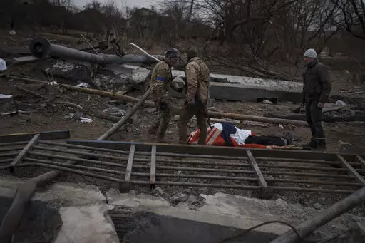 The body of a civilian, whose cause of death is unknown, lays on a stretcher on a path being used as an evacuation route out of Irpin, on the outskirts of Kyiv, Ukraine, Saturday, March 12, 2022. Kyiv northwest suburbs such as Irpin and Bucha have been enduring Russian shellfire and bombardments for over a week prompting residents to leave their homes. (AP Photo/Felipe Dana)