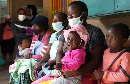 Women holding babies take their places on wooden benches at a clinic in Harare, Zimbabwe, Thursday, Sept. 15, 2022. Church members in Zimbabwe are getting their children vaccinated against measles in secret amid a deadly outbreak. It's to avoid being shunned by religious leaders who are opposed to modern medicine. (AP Photo/Tsvangirayi Mukwazhi)