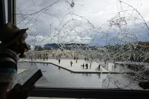 A protester, supporter of Brazil's former President Jair Bolsonaro, looks out from a shattered window of the Planalto Palace after he and many others stormed it, in Brasilia, Brazil, Jan. 8, 2023. Members of the three branches of power in Brazil say the country’s democracy and its guardrails have been restored after the trashing of the government buildings a year ago. But arrests have led supporters of the former president to say their freedom of speech is being violated and claim they are pol