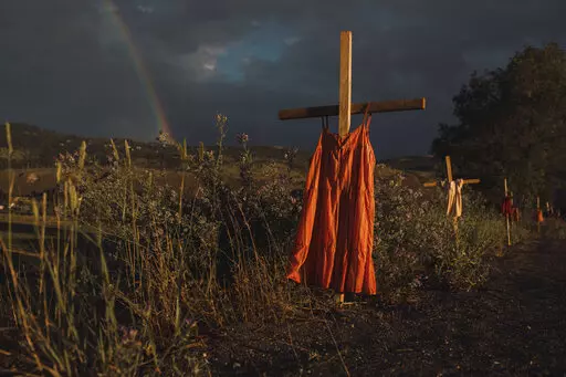 This image provided by World Press Photo which won the World Press Photo Of The Year award by Amber Bracken for The New York Times, titled Kamloops Residential School, shows Red dresses hung on crosses along a roadside commemorate children who died at the Kamloops Indian Residential School, an institution created to assimilate Indigenous children, following the detection of as many as 215 unmarked graves, Kamloops, British Columbia, 19 June 2021. (Amber Bracken for The New York Times/World Press