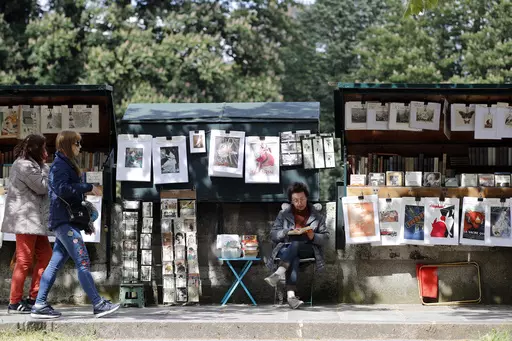 Visitors walk past a bookseller of used and antiquarian books called "Bouquiniste", in Paris, Thursday, May 10, 2018. French President Emmanuel Macron has revealed his bookish side and abandoned plans Tuesday, Feb. 13, 2024, to move the famed second-hand bookseller boxes flanking the banks of the Seine that are beloved by tourists, in preparation for July's Olympics opening ceremony in Paris. (AP Photo/Christophe Ena, File)