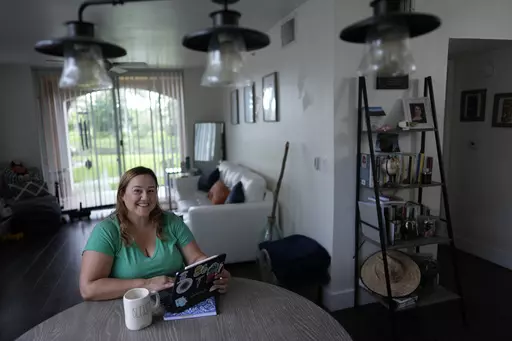 Melissa Lombana, 43, a high school teacher and mountain bike enthusiast, poses for a picture while working online, in her one-bedroom apartment in Miramar, Fla., Wednesday, July 26, 2023. Lombana's rent has increased each of the last two years and now amounts to nearly half her monthly income. "In a year, I will not be able to afford living here at all," she said. (AP Photo/Rebecca Blackwell)