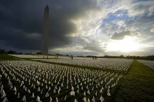 With the Washington Monument in the background, people look at white flags that are part of artist Suzanne Brennan Firstenberg's temporary art installation, "In America: Remember," in remembrance of Americans who have died of COVID-19, on the National Mall in Washington, Sept. 17, 2021. The installation consists of more than 630,000 flags. The federal government has provided more than $2 billion to help cover funeral costs for more than 300,000 families of people who died from COVID-19, the Fede