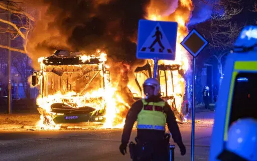 Riot police watch a city bus burn on a street in Malmo, Sweden, Saturday, April 16, 2022. Unrest broke out in southern Sweden late Saturday despite police moving a rally by an anti-Islam far-right group, which was planning to burn a Quran among other things, to a new location as a preventive measure. (Johan Nilsson/TT via AP)
