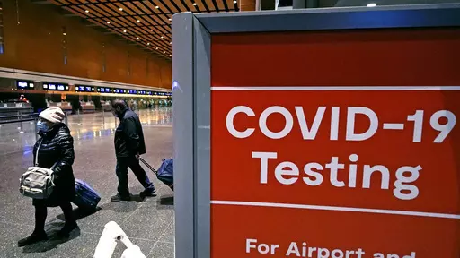 Travelers pass a sign near a COVID-19 testing site in Terminal E at Logan Airport, on Dec. 21, 2021, in Boston. The nation’s top public health agency is expanding a program that tests international travelers for COVID-19 and other infectious diseases. The Centers for Disease Control and Prevention currently operates a program at six U.S. airports that asks passengers from inbound international flights to agree to nose swabs and answer questions about their travel. (AP Photo/Charles Krupa, File