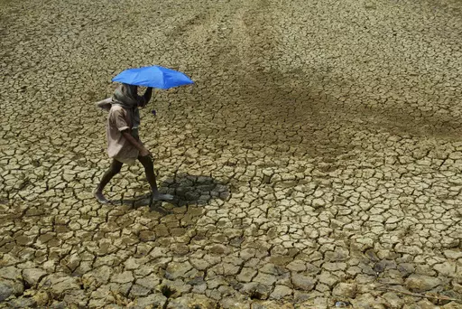 A villager holding umbrella to protect himself from sun, walks over parched land on the outskirts of Bhubaneswar, India on May 2, 2009. Tense negotiations at the final meeting on a climate-related loss and damages fund — an international fund to help poor countries hit hard by a warming planet — ended Saturday, Nov. 4, 2023, in Abu Dhabi, with participants agreeing that the World Bank would temporarily host the fund for the next four years.(AP Photo/Biswaranjan Rout, File)