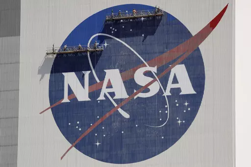 Workers on scaffolding repaint the NASA logo near the top of the Vehicle Assembly Building at the Kennedy Space Center in Cape Canaveral, Fla., May 20, 2020. (AP Photo/John Raoux, File)