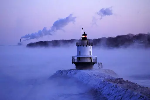Spring Point Ledge Light is surrounded by arctic sea smoke while emissions from the Wyman Power plant, background, are blown horizontal by the fierce wind, Saturday, Feb. 4, 2023, in South Portland, Maine. The morning temperature was about -10 degrees Fahrenheit. (AP Photo/Robert F. Bukaty)