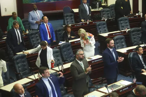 Rep. Carlos Guillermo Smith, D-Orlando (blue suit, in back) yells his objection as Republicans in the House of Representatives applaud after Senate Bill 4C Independent Special Districts, which affects Disney, passes Thursday, April 21, 2022 at the Capitol in Tallahassee, Fla. The session was halted on a protest by Democrats, but continued after a brief recess. (AP Photo/Phil Sears)