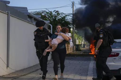 Israeli police officers evacuate a woman and a child from a site hit by a rocket fired from the Gaza Strip, in Ashkelon, southern Israel, Saturday, Oct. 7, 2023. Israel and Hamas have both been accused of breaking the rules of armed conflict. Hamas killed hundreds of civilians and abducted scores more when it attacked southern Israel on Oct. 7. Israel has bombarded Gaza and told more hundreds of thousands of Palestinians to leave their homes. The United Nations says it is collecting evidence of 