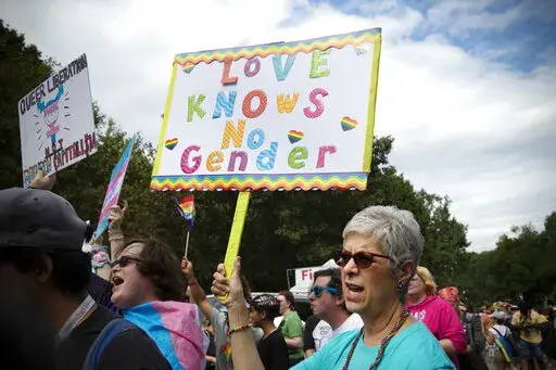 Barbara Dale, from Atlanta, mother of a transgender child, waves sign reading "Love Knows No Gender" at Gay Pride Transgender March at Piedmont Park in the city's Midtown District in Atlanta, Ga, Saturday, Oct. 12, 2019. Transgender medical treatment for children and teens is increasingly under attack in many states, labeled child abuse and subject to criminalizing bans. But it has been available in the United States for more than a decade and is endorsed by major medical associations. (AP Photo