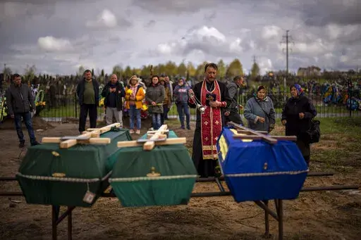 A priest blesses the remains of three people who died during the Russian occupation and were disinterred from temporary burial sites in Bucha, on the outskirts of Kyiv, on Wednesday, April 27, 2022. (AP Photo/Emilio Morenatti)