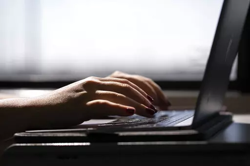 A woman types on a laptop while on a train in New Jersey, May 18, 2021. A trial of a four-day workweek in Britain, billed as the world's largest, has found that an overwhelming majority of the 61 companies that participated over six months last year will keep going with the shorter hours and that most employees were less stressed and burned out and had better work-life balance. (AP Photo/Jenny Kane, File)