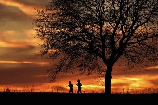 People are silhouetted against the sky at sunset as they run in a park, Nov. 12, 2024, in Shawnee, Kan. (AP Photo/Charlie Riedel, File)