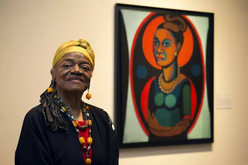 Artist Faith Ringgold poses for a portrait in front of a painted self-portrait during a press preview of her exhibition, "American People, Black Light: Faith Ringgold's Paintings of the 1960s" at the National Museum of Women in the Arts in Washington, June 19, 2013. Ringgold, an award-winning author and artist who broke down barriers for Black female artists and became famous for her richly colored and detailed quilts combining painting, textiles and storytelling, died Friday, April 12, 2024, at
