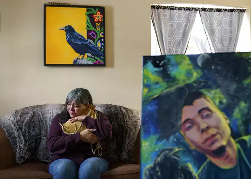 Rachel Taylor clutches a buckskin satchel filled with the ashes of her son, Kyle "Little Crow" Domrese, pictured at right, who died of an overdose, as she sits in the home they shared in Bemidji, Minn., Wednesday, Nov. 17, 2021. Just weeks remained until the anniversary of the day she opened his bedroom door and found her son face-down on his bed, one of more than 100,000 Americans lost in a year to overdoses as the COVID-19 pandemic aggravated America's addiction disaster. The death rate from d